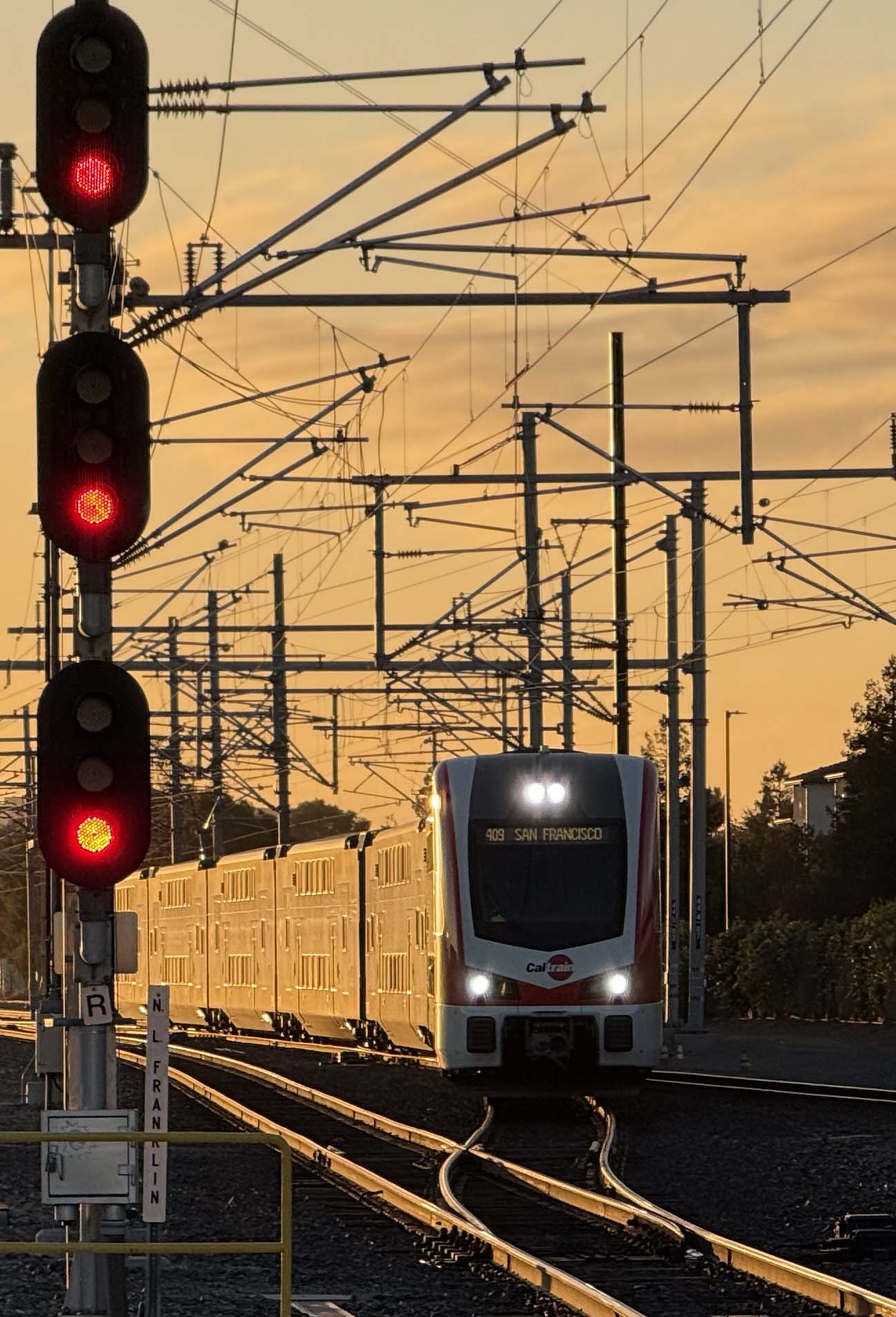A new electric Caltrain arriving under the overhead wires at sunset